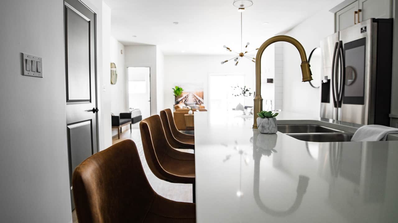 Cocina moderna con isla blanca, taburetes de cuero marrón, grifo dorado y electrodomésticos de acero inoxidable en Tomelloso