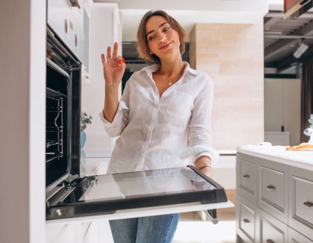 Mujer cocinando y revisando el horno en una cocina blanca moderna a medida en Tomelloso